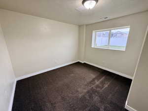 Empty room with dark carpet and a textured ceiling