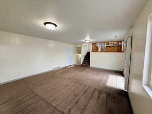 Empty room featuring carpet floors, a textured ceiling, and stairs
