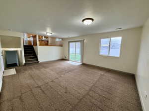 Unfurnished living room featuring a textured ceiling, carpet flooring, and stairs