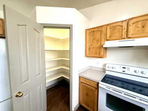 Kitchen with white appliances, light countertops, under cabinet range hood, dark wood-type flooring, and brown cabinetry