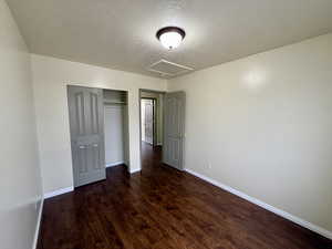 Unfurnished bedroom with attic access, a textured ceiling, a closet, and dark wood-style flooring
