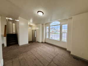 Empty room featuring stairs, a textured ceiling, and carpet