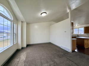 Unfurnished room featuring vaulted ceiling, a textured ceiling, and dark colored carpet