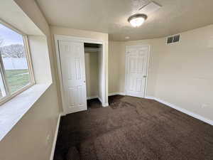 Unfurnished bedroom featuring dark carpet, a closet, and a textured ceiling