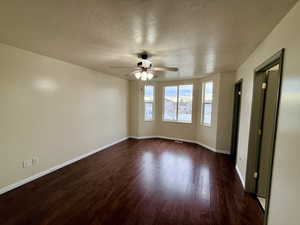 Unfurnished room with a textured ceiling, dark wood-style flooring, and a ceiling fan