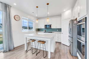 Kitchen featuring appliances with stainless steel finishes, white cabinetry, pendant lighting, a kitchen island with sink, and a breakfast bar