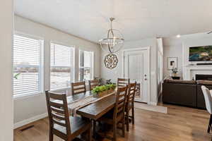Dining room featuring light wood finished floors, a textured ceiling, a lit fireplace, and a chandelier