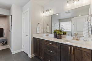 Ensuite bathroom with double vanity, dark tile patterned flooring, and a textured ceiling
