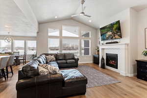Living room with light wood-type flooring, a tile fireplace, ceiling fan, a chandelier, and healthy amount of natural light