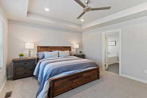 Bedroom with a tray ceiling, ceiling fan, connected bathroom, light carpet, and recessed lighting