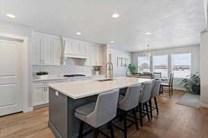 Kitchen with white cabinets, hanging light fixtures, a textured ceiling, a kitchen island with sink, and a chandelier