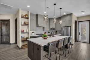 Kitchen featuring a kitchen bar, a center island with sink, hanging light fixtures, gray cabinetry, and recessed lighting