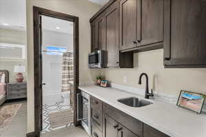 Kitchen featuring dark brown cabinets, light stone counters, wine cooler, stainless steel microwave, and light tile patterned flooring