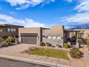 View of front of house featuring a pergola, driveway, stucco siding, and an attached garage