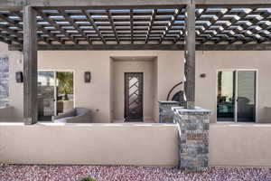 View of exterior entry with a patio, a pergola, and stucco siding