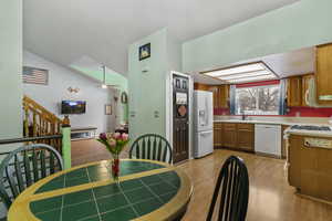 Dining room with ceiling fan, light wood-style flooring, vaulted ceiling, and stairs