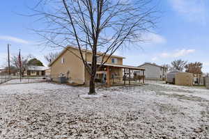 Snow covered rear of property with a fenced backyard, a patio, and a storage unit