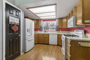 Kitchen with white appliances, brown cabinets, light countertops, and light wood-style flooring
