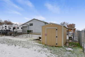 Snow covered structure featuring a fenced backyard, a gate, and a shed