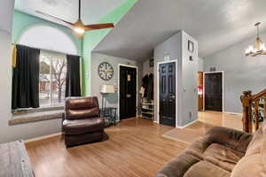 Living area with light wood-style floors, a chandelier, a ceiling fan, vaulted ceiling, and a textured ceiling