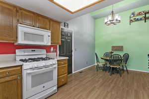 Kitchen featuring white appliances, brown cabinetry, pendant lighting, a chandelier, and light wood-style flooring
