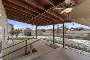 Snow covered patio with ceiling fan, a residential view, a storage shed, and a patio
