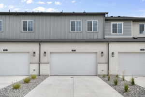View of front facade with board and batten siding, stone siding, driveway, and an attached garage
