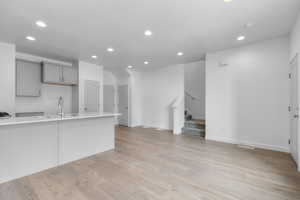 Kitchen with recessed lighting, gray cabinets, light wood-type flooring, light stone countertops, and open floor plan