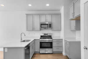 Kitchen with stainless steel appliances, gray cabinets, a peninsula, recessed lighting, and light stone counters