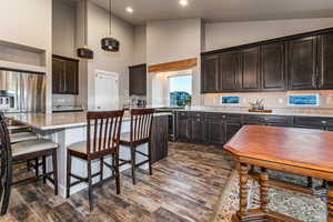 Kitchen with dark brown cabinets, an island with sink, light stone counters, stainless steel gas stove, and a kitchen breakfast bar