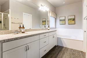 Full bathroom with double vanity, dark wood-type flooring, a garden tub, and a stall shower