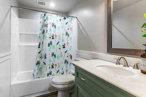 Full bath with shower / bath combo, vanity, wainscoting, and a textured ceiling
