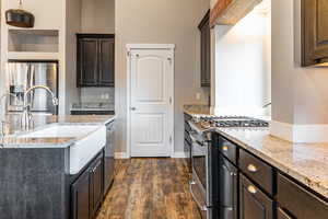 Kitchen with dark brown cabinets, appliances with stainless steel finishes, light stone counters, and dark wood-type flooring