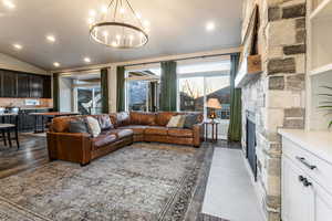 Living room with recessed lighting, lofted ceiling, a stone fireplace, and dark wood-type flooring