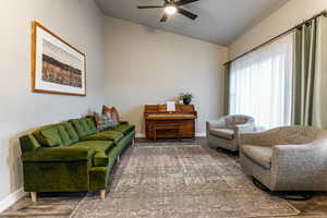 Living room featuring vaulted ceiling, ceiling fan, and dark wood-type flooring