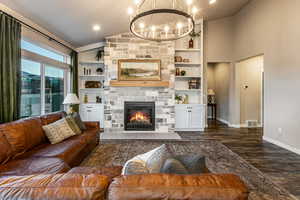Living area with lofted ceiling, built in shelves, dark wood finished floors, a stone fireplace, and a chandelier