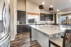 Kitchen with a breakfast bar, stainless steel appliances, light stone countertops, dark brown cabinets, and high vaulted ceiling