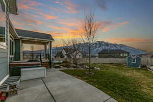 Yard at dusk featuring a trampoline, a shed, a fenced backyard, and a mountain view