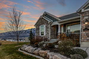 Property exterior at dusk with board and batten siding, stone siding, covered porch, a yard, and a mountain view