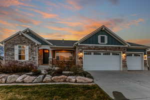 Craftsman-style house featuring board and batten siding, stone siding, covered porch, concrete driveway, and a garage