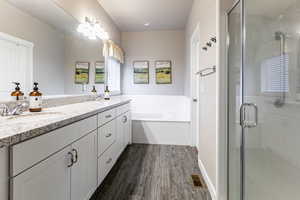 Full bathroom with double vanity, a bath, a stall shower, and dark wood-style floors