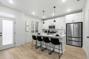 Kitchen with stainless steel appliances, a breakfast bar, white cabinets, pendant lighting, and a kitchen island with sink