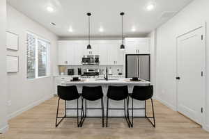 Kitchen featuring white cabinets, a kitchen bar, decorative light fixtures, an island with sink, and recessed lighting