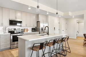 Kitchen featuring stainless steel appliances, decorative light fixtures, an island with sink, a breakfast bar, and light wood-style flooring