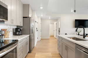 Kitchen featuring gray cabinetry, stainless steel appliances, decorative light fixtures, light wood finished floors, and light stone countertops