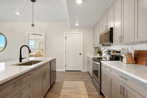 Kitchen with gray cabinets, appliances with stainless steel finishes, hanging light fixtures, light wood-style flooring, and light stone countertops