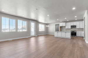 Unfurnished living room with hanging lights, a textured ceiling, and light wood finished floors