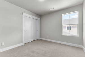 Unfurnished bedroom with light carpet, a closet, and a textured ceiling