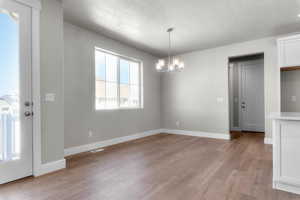 Unfurnished dining area with light wood-style flooring, a textured ceiling, and a chandelier
