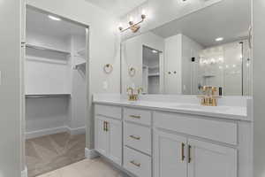 Full bath with a spacious closet, double vanity, a shower stall, and light marble finish floors
